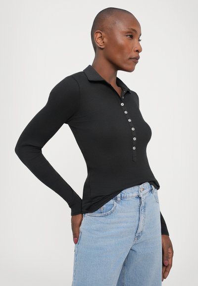 Black long-sleeve polo shirt with ribbed texture, featuring a placket of five buttons, paired with light blue high-waisted jeans.