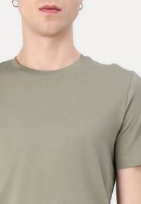 Ελαιόλαδο πράσινη κοντομάνικη μπλούζα φτιαγμένη από μαλακό βαμβάκι. Διαθέτει κλασικό λαιμόκοψη και απαλή υφή, κατάλληλη για καθημερινή χρήση.