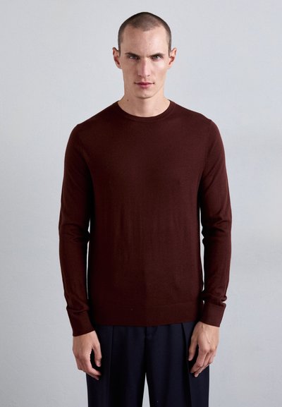 Mørkerød langærmet sweater vist på en model, med rund halsudskæring, tætsiddende design og glat tekstur, parret med mørke bukser.