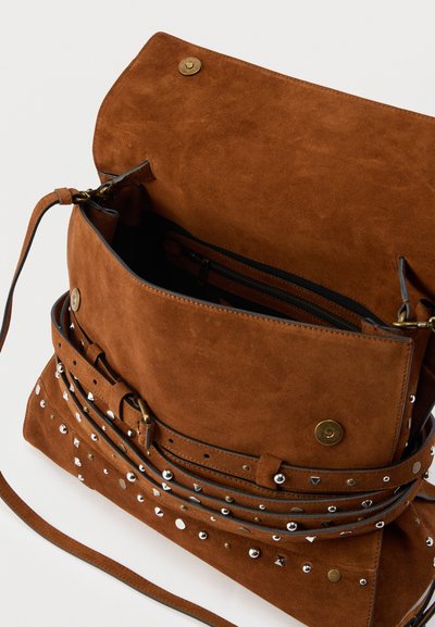 Καφέ τσάντα από σουέντ με καπάκι ανοιχτό, διακοσμημένη με ασημί και χρυσά καρφιά, και λεπτό ιμάντα ώμου.