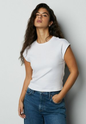 White short-sleeve t-shirt with a crew neck, made of smooth fabric. Paired with high-waisted blue denim jeans.