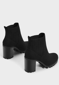 Black ankle boots with a textured fabric upper, elastic side panels, and a chunky, ridged heel. Close-toe design with a smooth finish.