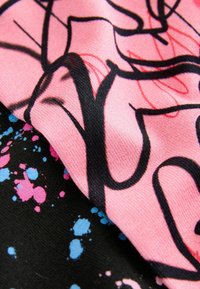 Satinfabriker, en rosa med svarta klottrade linjer, en annan svart med blå och rosa sprutmönster, visade överlappande.