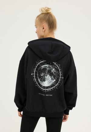 Un sweat à capuche noir avec un grand imprimé céleste blanc au dos, présentant des motifs de lune et d'étoiles. Coupe ample avec un cordon de serrage pour la capuche.
