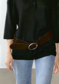 Person wearing light blue jeans and a black knit sweater with a wide brown belt fastened loosely around the waist.