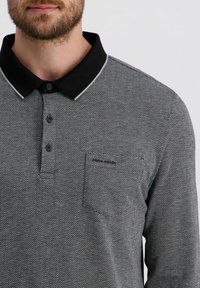 Polohemd in Schwarz und Grau mit Fischgrätmuster, schwarzem Kragen, zwei Knöpfen und einer Brusttasche aus strukturiertem Stoff.