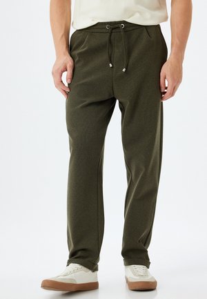 Olijfgroene jogpants van een textuurstof, met een elastische tailleband, koord en zijzakken, gecombineerd met witte sneakers.
