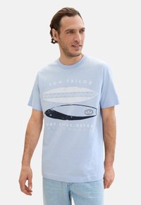 Světle modré tričko s grafikou surfového prkna v černé barvě, s textem "TOM TAILOR" a "SURF.CHILL.REPEAT" v bílé barvě. Krátké rukávy, kulatý výstřih.