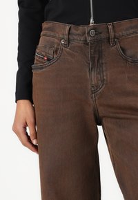 Brown denim jeans with a slight distressed texture. Features front pockets with a branded tag and a zipper top closure.