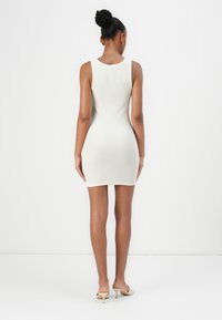 Λευκό ριγέ αμάνικο φόρεμα με εφαρμοστό σχήμα, μήκος μέχρι το γόνατο και λεία υφή. Η πίσω όψη επισημαίνει έναν απλό, καθαρό σχεδιασμό.