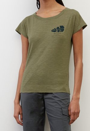 Kvinde iført en olivengrøn T-shirt med en lille mørkegrøn bladgrafik og tekst på brystet, kombineret med grå cargobukser.