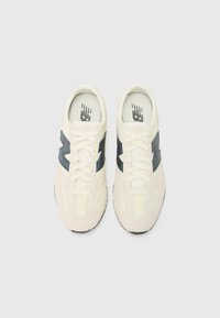 New Balance sneakers in cream and navy, featuring a suede and mesh texture, lace-up design, and a contrasting logo on the side.