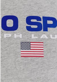 Šedá bavlněná textilie s výrazným modrým a bílým textem. V dolní části malý potisk americké vlajky.