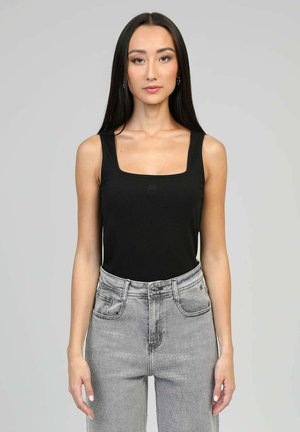 Femme aux longs cheveux foncés porte un haut noir sans manches à encolure carrée et un jean gris taille haute avec un motif à petits pois subtil.