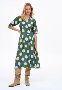 Zelené šaty s volným střihem, velkými bílými a modrými puntíky, krátkými rukávy a rozšířenou sukní. V kombinaci s béžovými volnými kozačkami až ke kolenům.