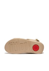 Beige sandaal met een gestructureerde rubberen zool, met een verhoogd "fitflop" logo en een rode cirkelaccent op de hiel. Verstelbare banddetailing.