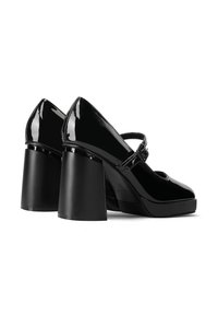 Le scarpe con tacco alto in vernice nera presentano una punta rotonda e un tacco a blocco. Le scarpe hanno una cinghia con una fibbia che mette in risalto il design.