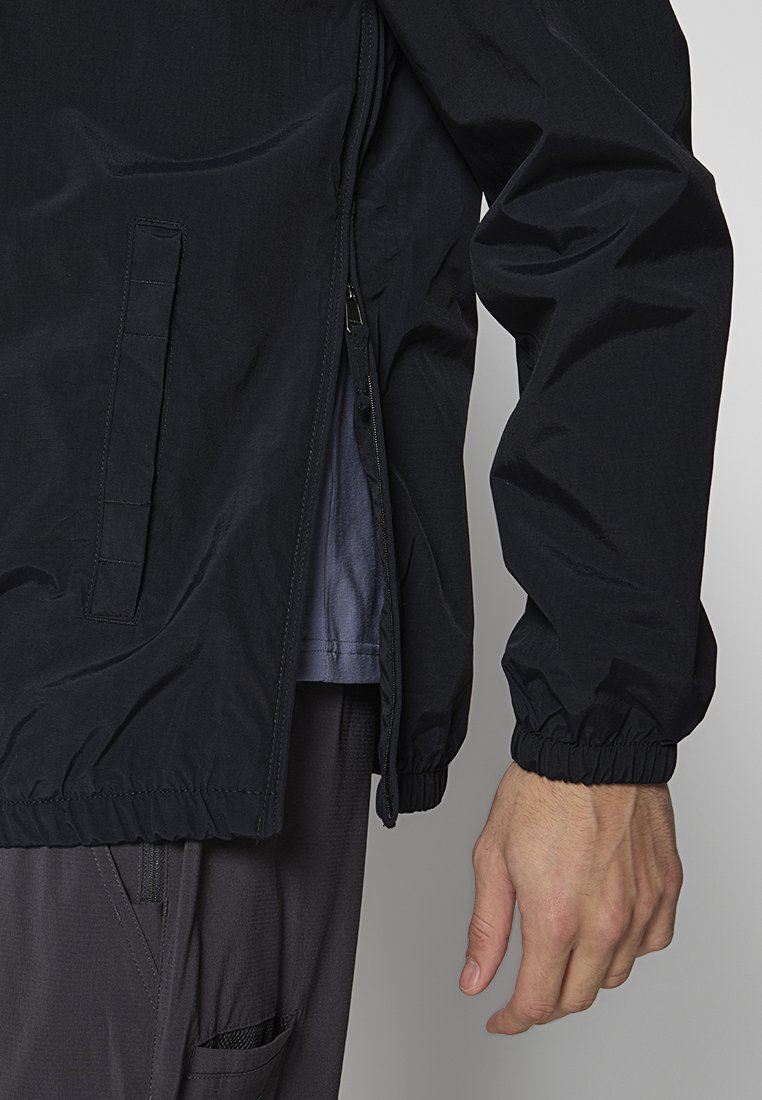 Zwarte lichtgewicht jas met ritssluiting, elastische manchetten en zijzak. Gladde textuur, casual ontwerp, geschikt voor verschillende temperaturen.