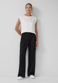 Haut blanc à manches courtes avec un col rond, associé à un pantalon noir taille haute et des baskets blanches, créant un look monochrome épuré.