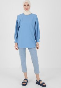 Maglietta azzurra chiara a maniche lunghe con scollatura quadrata, maniche arricciate, abbinata a jeans in denim chiaro e sandali blu navy.