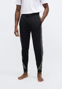 Čierne tepláky s opaskom na šnúrku, bočnými pásikmi a rebrovanými manžetami. Vyrobené z mäkkej látky s priliehavým strihom.