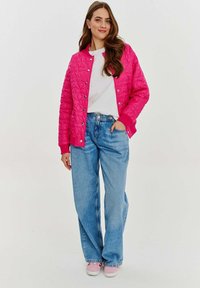 Kvalitná prešívaná ružová bomber bunda so západkami, nosená cez biele tričko, skombinovaná so svetlomodrými širokými nohavicami a ružovými teniskami.