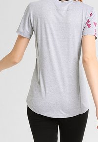 Graues Sport-T-Shirt mit kurzen Ärmeln, glatter Textur, geschwungener Saumlinie und rosa Blumenakzenten an den Schultern. Schlichtes Design.
