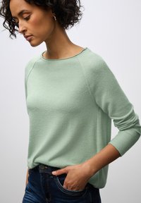 Maglione a maglia verde chiaro con scollatura rotonda e maniche raglan, abbinato a jeans blu scuro. Texture liscia, vestibilità casual.