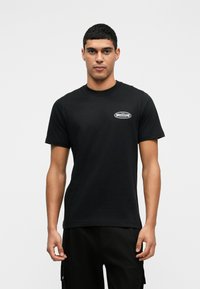 Schwarzes Baumwoll-T-Shirt mit kurzen Ärmeln und rundem Halsausschnitt. Verfügt über ein kleines weißes Logo auf der linken Brust. Glatte Textur, lässige Passform.