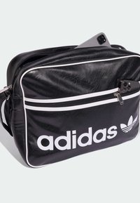 Melnas mākslīgās ādas soma ar baltiem akcentiem, ar rāvējslēdzēja kabatu un izteiksmīgu "adidas" logo. Piedāvā strukturētu taisnstūra formu un regulējamu siksnu.