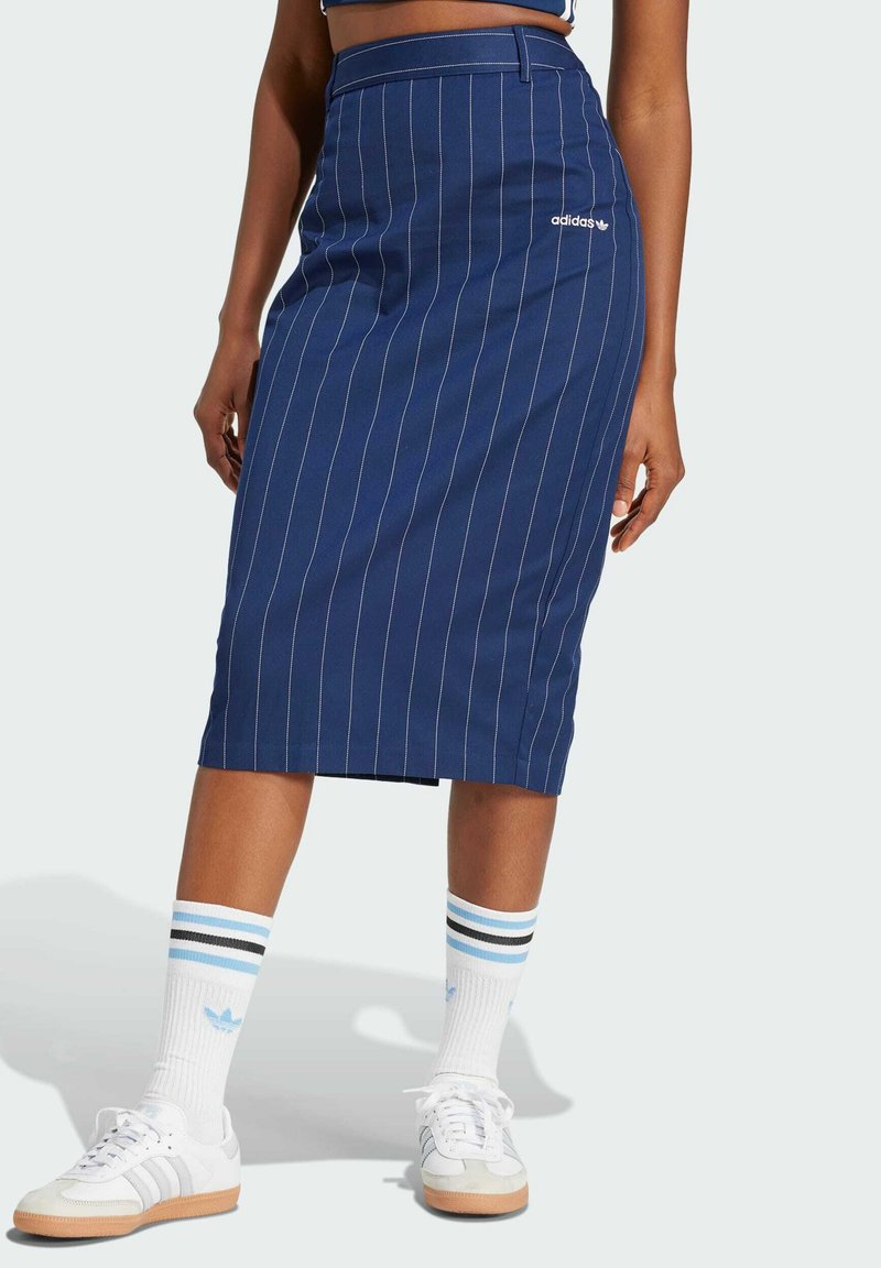 Marinblå blyertskjol med vita randiga detaljer, medellång design, med ett varumärkeslogotyp. Matchad med vita sneakers och randiga strumpor.