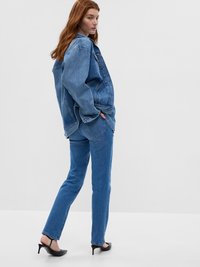 Veste en denim bleu et jeans. La veste est surdimensionnée avec une coupe décontractée, et les jeans sont à jambe droite. Des chaussures à talons hauts noires complètent le look.
