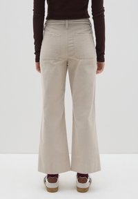 Beige, wijde corduroy broeken met een gestructureerd oppervlak, achterzakken en een hoge taille. Gecombineerd met witte sneakers en bordeauxrode sokken.
