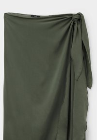 Jupe portefeuille vert olive avec un détail de nœud sur le côté, tissu lisse et finition légèrement brillante.