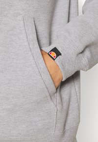 Grijze sweatshirt met geribbelde boorden en zak. Voorzien van een merklabel met rode, zwarte en oranje accenten op de mouw. Zachte textuur.
