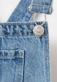 Světle modré džínové lacláče s kovovou stříbrnou sponou a zapínáním na knoflíky, s viditelným šitím a přední kapsou.