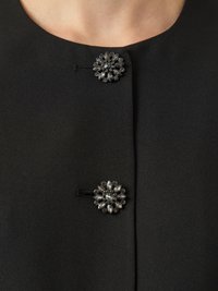 Black jacket featuring two decorative floral brooches with clear and dark gem accents, set in a smooth, structured textile.