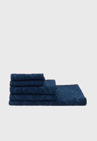 Pile de cinq serviettes bleu marine pliées avec motifs floraux embossés sur un fond blanc uni.