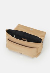 Beige crossbody-väska gjord av slät syntetiskt material med en enkel magnetstängning, svart inredning och en extern ficka med dragkedja.