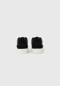Black sneakers with a suede and leather upper, white rubber sole. Features rounded design and smooth texture. Branding visible on heel.