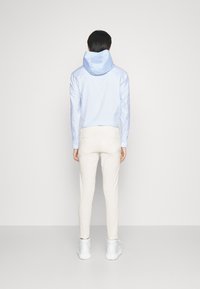 Jasnoniebieska koszula zapinana na guziki z kapturem, z paskowanymi rękawami. W połączeniu z kremowymi, obcisłymi spodniami i białymi trampkami.