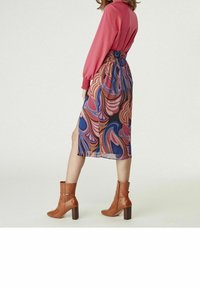 Bohemisk klänning med ett livfullt, virvlande mönster i orange, lila och blått. Kombinerad med bruna, klackade ankelstövlar.