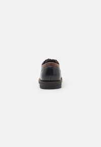 Black and brown leather shoe with a rounded toe, contrasting heel, and visible stitching detail. Leather upper with a wooden sole.