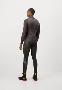 Sort langærmet top og leggings med et geometrisk mønster, der har et tætsiddende design og struktureret stof. Sorte sko med gule accenter.