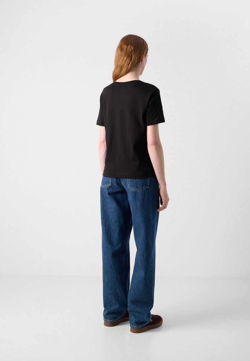 Czarna krótka koszulka z okrągłym dekoltem w połączeniu z luźnymi niebieskimi dżinsami. Dżinsy mają klasyczny pięciopocketowy krój.