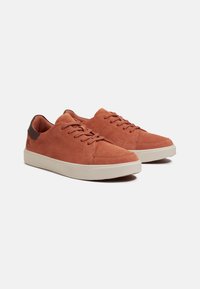 Sneakers in suede color ruggine con tallone in pelle marrone liscia, caratterizzati da un design con lacci e suola in gomma bianca a contrasto.