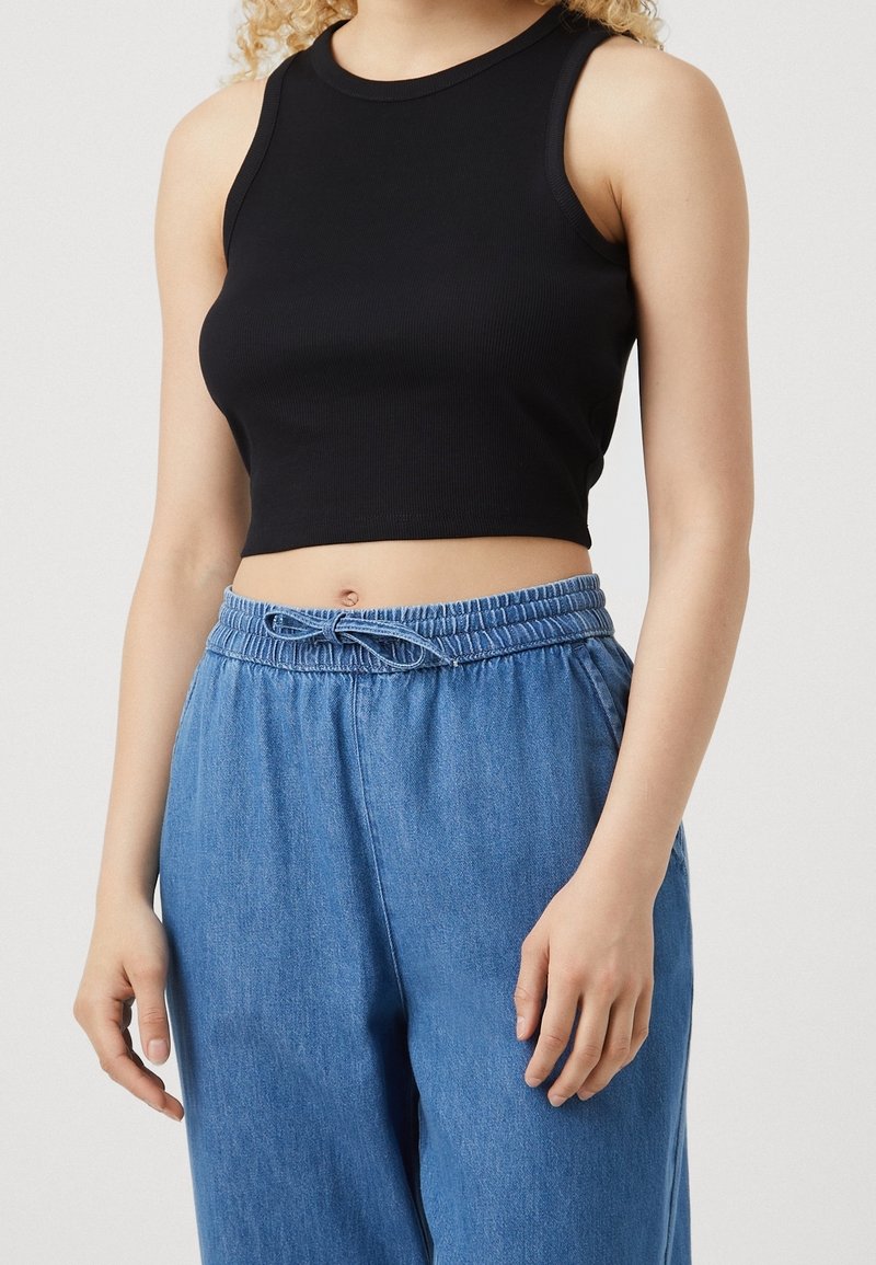 Black ribbed crop top with a round neckline. Paired with loose-fitting blue denim pants featuring an elastic waistband and drawstring.