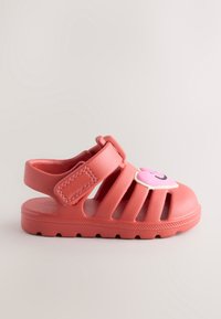 Rosa Gummisandale mit geschlitztem Design, verstellbarem Riemen und einem lächelnden Charaktergrafik auf dem Zehenbereich. Strukturierte Sohle für besseren Halt.