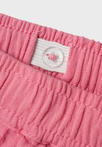 Ceinture en tissu rose avec des plis texturés, dotée d'un bouton transparent et d'un espace pour une étiquette blanche. Texture lisse avec un léger éclat.