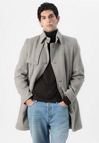 Grau melierter Woll-Mix-Mantel mit Kragen und Knopfverschluss, getragen über einem schwarzen Rollkragenpullover. Kombiniert mit blauen Jeans aus Denim in lässiger Passform.